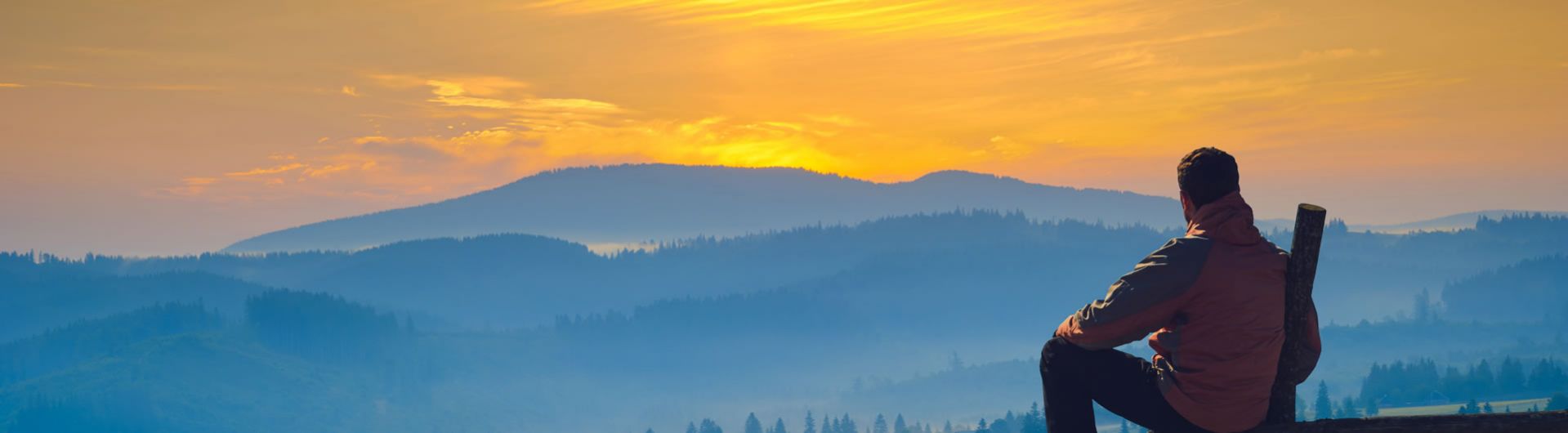 man in jacket watching sunset over valley